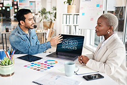 Ocean County SEO professional having a meeting with a client with a laptop on a desk that have blue glowing letters SEO